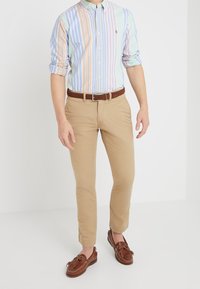 Gestreepte shirt voor mannen in pastelkleuren, khaki broek en bruine boat shoes. Heeft een kraag, lange mouwen en een leren bruine riem.