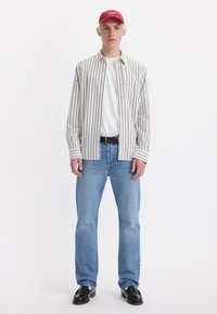 Striped button-up shirt with a white base and gray stripes, paired with a white t-shirt, blue jeans, and a red cap, featuring black shoes.