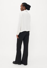 Blouse blanche à manches longues avec un col, assortie à un pantalon noir évasé. Texture de tissu lisse ; la coupe décontractée met en valeur la silhouette.