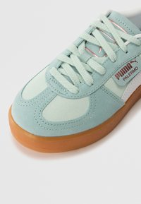 Svijetloplave suknene tenisice s gumiranim potplatom, koje imaju ravne vezice i bijelu bočnu prugu. Istaknuti "PUMA PALERMO" logotip u crvenoj boji.