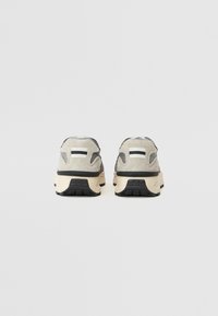 Calzature con una tomaia grigia in suede e mesh, con una intersuola crema e una suola in gomma nera. Include una striscia di accento nera.