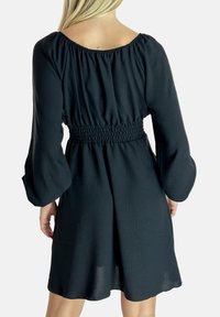 Schwarzes Kleid mit langen Puffärmeln, gerafftem Taillendetail und lockerer Passform. Leichter Stoff mit subtiler Textur. Quadratischer Ausschnitt.