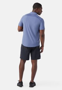 Korte mouwen, lichtblauwe polo met een subtiele textuur, gecombineerd met zwarte shorts. De polo heeft een kraag en een ronde zoom.