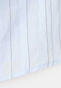 Tissu blanc avec fines rayures verticales noires et motifs tricotés texturés subtils en gros plan.