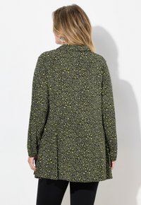 Tunika a maniche lunghe di colore verde scuro con una distintiva stampa animale gialla, con orlo leggermente svasato e colletto. Tessuto morbido al tatto.