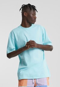 Light blue cotton t-shirt with a crew neck and short sleeves, featuring minimalist white stitching on the chest. Smooth texture.