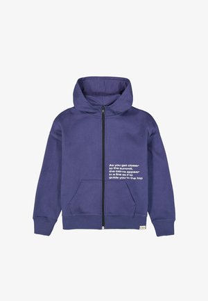 Lilla hættejakke med lynlås, forlommer og hvid tekst på højre bryst, der indeholder et motiverende citat om at nå en top.