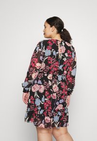 Vestido floral com fundo preto, mangas longas e padrões coloridos de flores vermelhas, rosas e azuis, com detalhe nas costas em forma de chave.