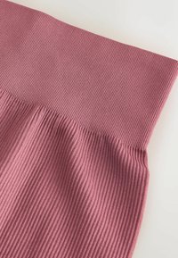 Csíkozott anyag, amely halvány mályva színű, széles, rugalmas derékkal és puha textúrával rendelkezik, egy világos háttér előtt, szögből bemutatva.