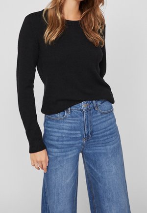 Pull en maille noir avec un col rond, associé à un jean large taille haute en denim clair présentant des nuances subtiles et des sections décolorées.