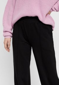 Black wide-leg pants with a soft texture and an elastic waistband, paired with a loose-knit, light pink sweater.