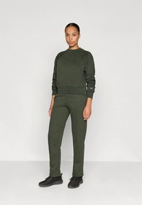 Ciemnozielona bluza i pasujące spodnie wykonane z miękkiego materiału. Bluza ma okrągły dekolt i prążkowane mankiety. Na rękawie znajduje się detal z logo.