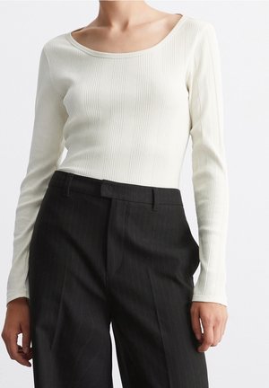 Woman wearing a fitted white ribbed long-sleeve top tucked into high-waisted black pinstripe trousers.