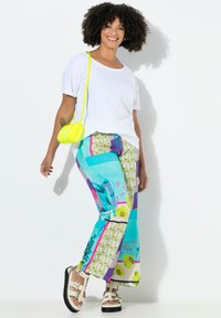 Fel gekleurde, wijde broek in turquoise met harten, stippen en levendige graphics. Combinatie met een wit shirt en een gele tas.