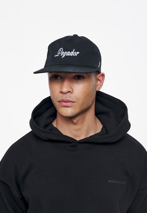 Black cap with "Pegador" embroidered in white, flat brim, made of fabric, worn with a black hooded sweatshirt featuring a subtle logo.