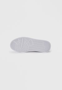 Hvit sneaker såle med teksturerte grep mønstre, inkludert sirkulære, sikksakk og lineære design mot en enkel hvit bakgrunn.