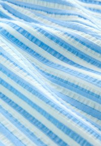 Tissu doux avec des rayures horizontales alternées bleu clair et blanc, présentant une texture subtile et des plis légers.