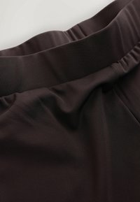 Gros plan d'un tissu brun foncé avec une ceinture élastique froncée, montrant la texture et les détails des coutures.