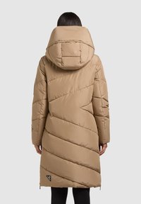 Dlouhý béžový prošívaný kabát s velkou, polstrovanou kapucí. Má diagonální prošívaný vzor, úzký střih a logo u lemu.