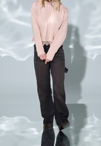 Svetle růžová zkrácená mikina s krajkovým lemem, spárovaná s černými volnými kalhotami. Hladká textilie, uvolněný siluet a dlouhé rukávy.