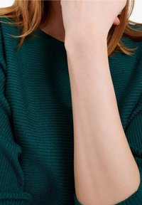 Turquoise geribbelde breisels met een zachte textuur, gedeeltelijk over een arm heen. Zichtbaar detail omvat het golfachtige patroon van het materiaal.