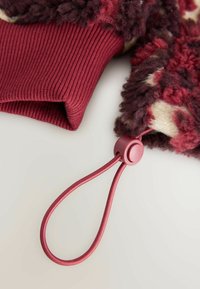 Przytulny burgundowy tekstylia z żeberkowanym mankietem, miękkim, fakturowanym wzorem w kremowych i ciemnych odcieniach oraz różowym regulowanym ściągaczem z okrągłym zatrzaskiem.