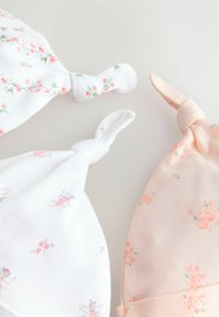Trois bonnets pour bébé en coton doux. Un blanc avec des motifs floraux roses, un blanc uni, et un pêche doux avec des accents floraux.