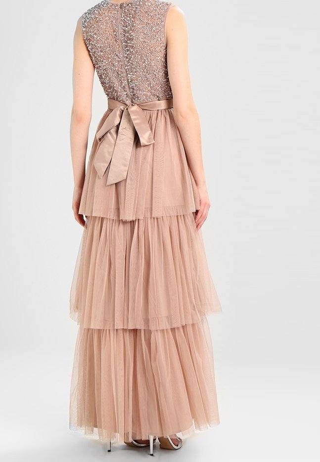 Femme portant une robe rose blush sans manches, longue jusqu'au sol, avec une jupe en tulle superposée, un corsage à sequins et un nœud en satin noué dans le dos.