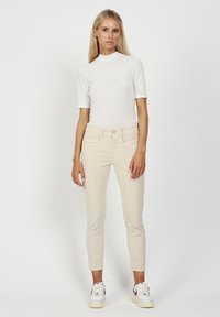 Light beige fitted jeans with a smooth texture and minimalistic design, paired with a short-sleeve white top. White sneakers complete the look.