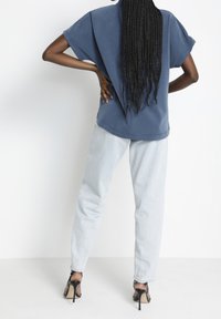 Blå oversized t-shirt med kort ärm, i kombination med ljusgrå jeans. Svarta högklackade skor framhäver outfiten.