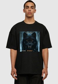 Black oversized t-shirt featuring a graphic of a fierce wolf's face with yellow eyes, text "Trust your instincts" and "be fearless!" in orange.