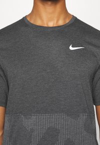Camiseta de manga corta de color gris oscuro, hecha de algodón, con un logo blanco de Nike en el pecho y un patrón texturizado en la parte inferior.