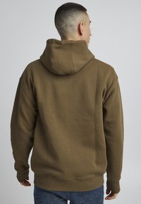 Brauner Kapuzenpullover mit strukturierter Oberfläche, elastischen Bündchen und geripptem Saum. Die Rückseite hat ein einfaches, nahtloses Design.