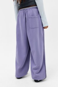 Calças largas roxas feitas de um tecido macio e texturizado; possuem um bolso traseiro e uma cintura elástica para conforto.