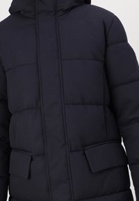 Mørkeblå dunjakke med hætte, quiltet design og to frontlommer. Fremstillet af et glat, holdbart stof med en blød tekstur.
