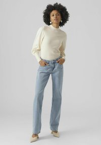 Maglione a costine color crema con maniche a palloncino, abbinato a jeans a gamba dritta blu chiaro e décolleté beige a punta. Accessori semplici.