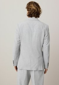 Blazer gris texturizado con un ajuste entallado, abertura simple en la parte posterior y acentos de botones en las mangas. Combina con pantalones grises de corte relajado.