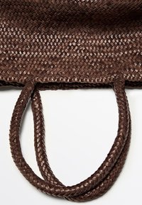Braune gewebte Ledertasche mit geflochtenen Griffen vor weißem Hintergrund, betont Textur und Handwerkskunst.
