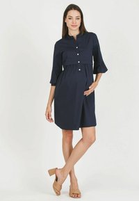 Abito premaman blu navy con chiusura a bottoni, maniche 3/4 e vita arricciata. Tessuto morbido e silhouette rilassata.
