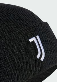 Berretto nero lavorato a maglia con texture a coste e un logo bianco prominente sul lato, che mostra un design aderente e arrotondato.