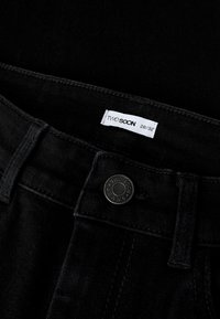 Svarta jeans i denim med enkel design, metallknapp med varumärke och en etikett som visar storlek 28/32. Texturerat tyg med minimal sömnad.