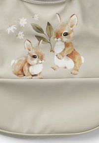 Beige väska med en tryckt illustration av två kaniner med brunt och vitt päls. Accenter inkluderar blommor och ett grönt blad. Slät textur.