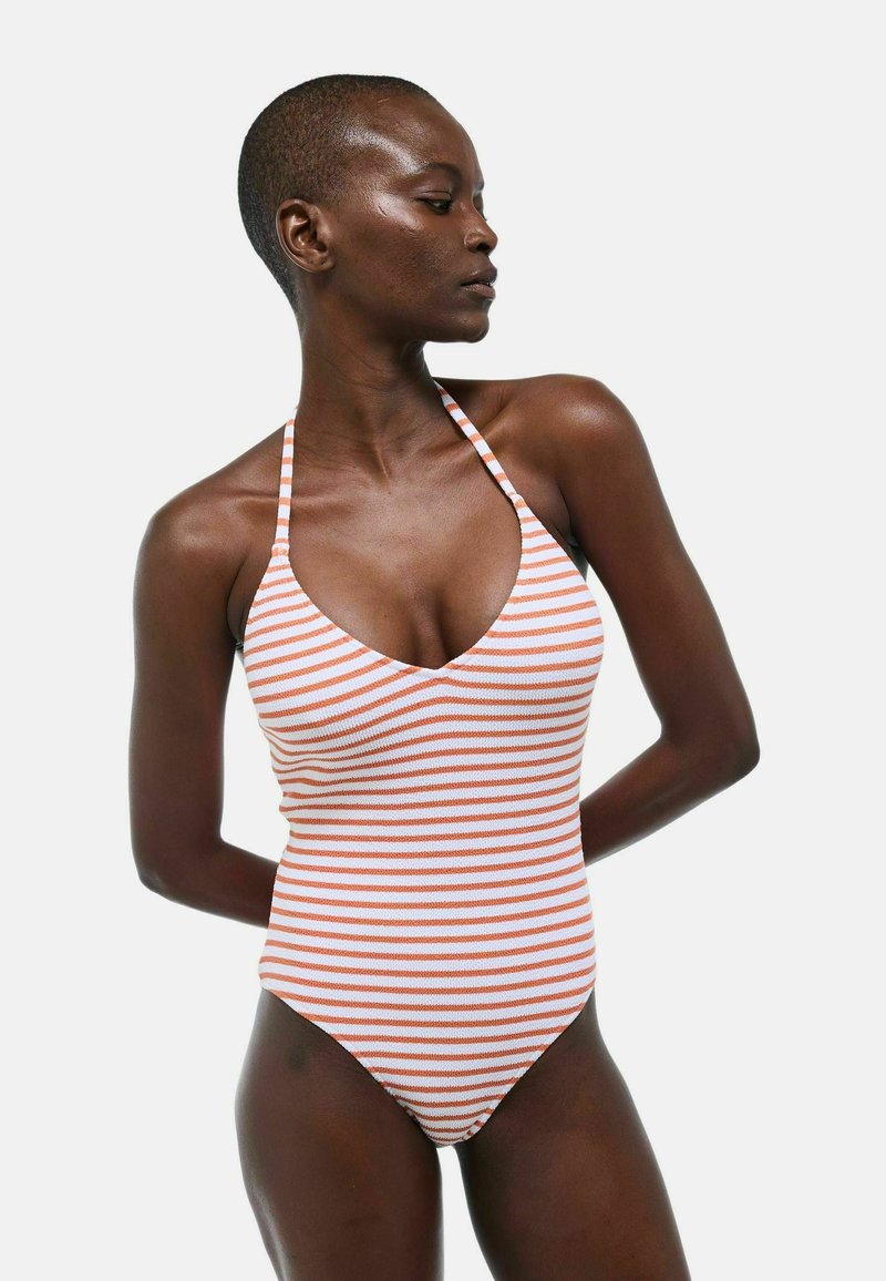 Maillot de bain une pièce rayé en blanc et orange, avec un décolleté plongeant et des bretelles autour du cou. Tissu lisse et extensible avec une silhouette ajustée.