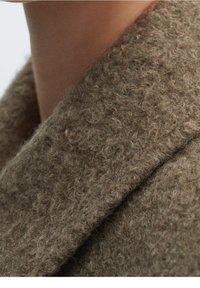 Brown woolen fabric with a soft, textured finish, featuring a wide collar and a seamless, cozy design. Close-up view of the material.