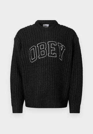 Juodas megztas megztinis su apvalia iškirpte, ant krūtinės išsiuvinėtas baltas užrašas „OBEY“. Visas megztinis dekoruotas reljefiniu raštu.