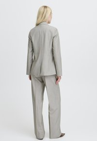 Svetlo sivi obleka z elegantnim srajčnim suknjičem in širokimi hlačnicami. Ima subtilne navpične črte in gladko teksturo. Brez dodatnih vidnih podrobnosti.