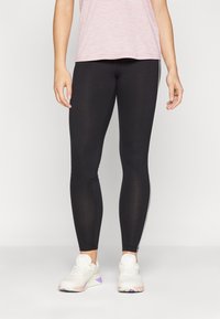 Sorte leggings med en tettsittende design, med hvite sidestipper. Kombinert med en lys rosa, løstsittende t-skjorte og hvite joggesko.