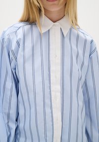 Mėlynos ir baltos horizontaliomis juostomis marškiniai su balta apykakle, turintys vertikalias juostas, įvairaus pločio. Mygtukų užsegimas priekyje. Lygi medžiagos tekstūra.