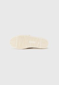 Såle i off-white gummi med et teksturert mønster av parallelle spor og sirkulære inntrykk. Har merkets logo tydelig preget.