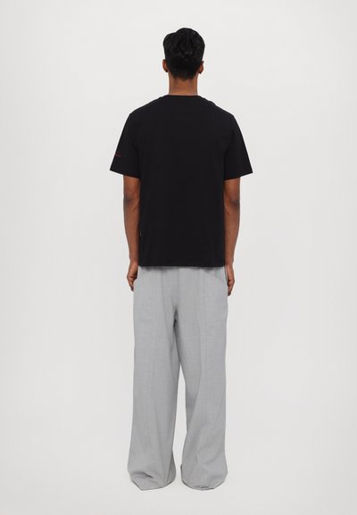 T-shirt en coton noir à manches courtes, associé à un pantalon large gris clair. Le t-shirt présente un accent subtil sur la manche.